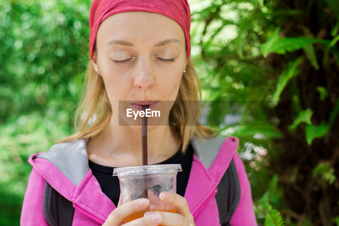 Woman with eyes closed drinking outdoors