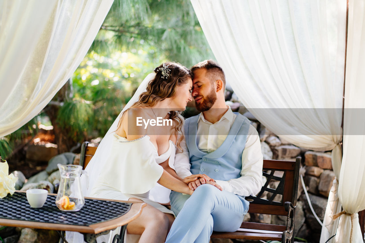 Newlywed bridegroom embracing while sitting outdoors