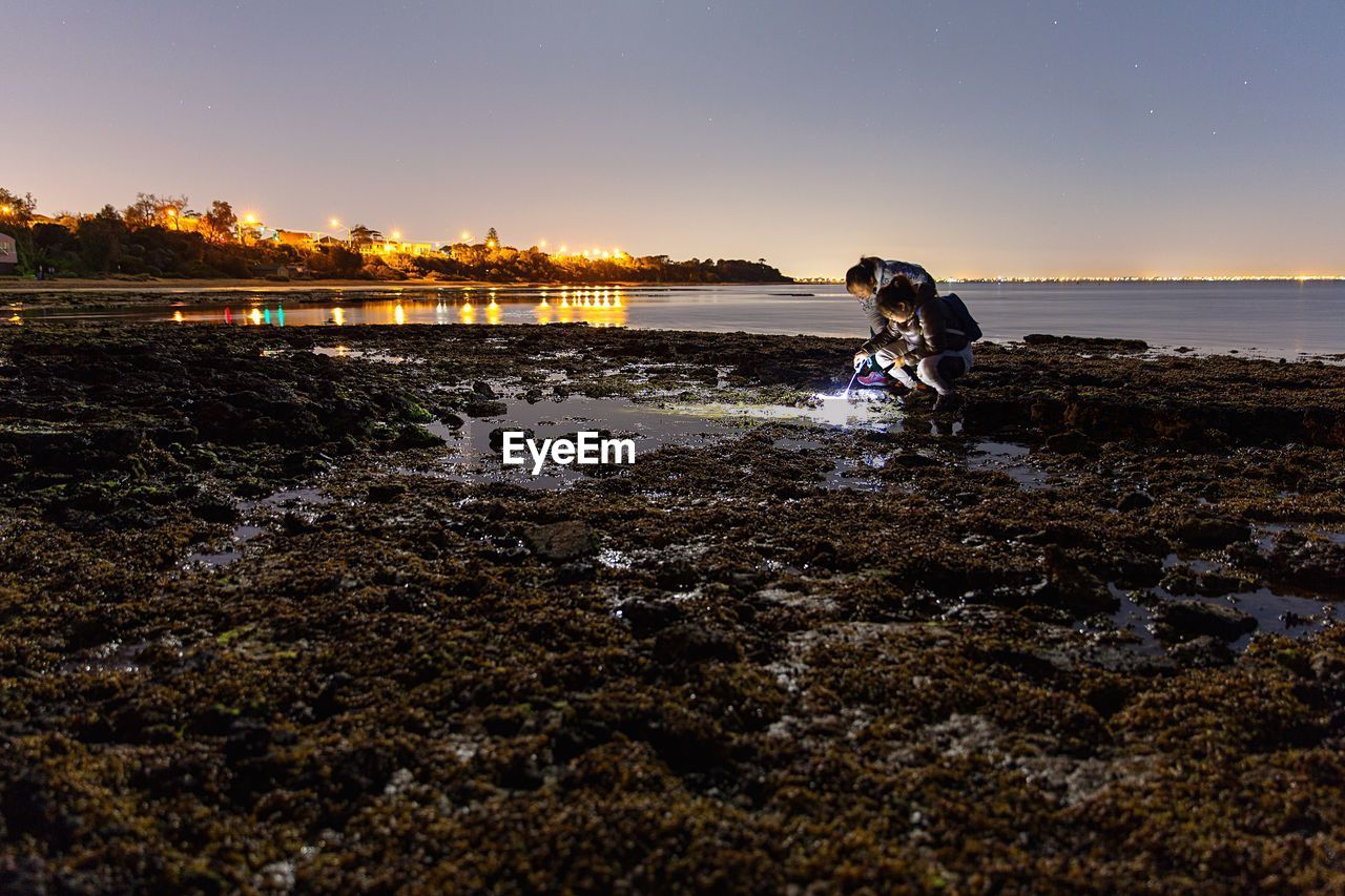 Women researching on rocky shore at night