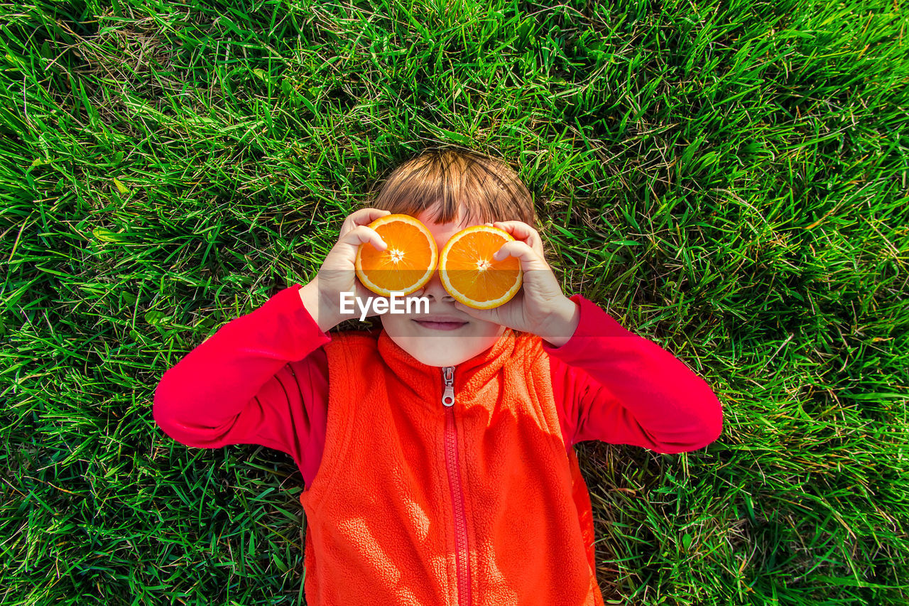 grass, one person, childhood, child, plant, yellow, green, front view, nature, holding, day, men, high angle view, leisure activity, portrait, casual clothing, field, standing, land, outdoors, fun, glasses, looking at camera, waist up, clothing, lifestyles, orange color, costume, smiling, innocence, red, person, disguise, happiness, flower