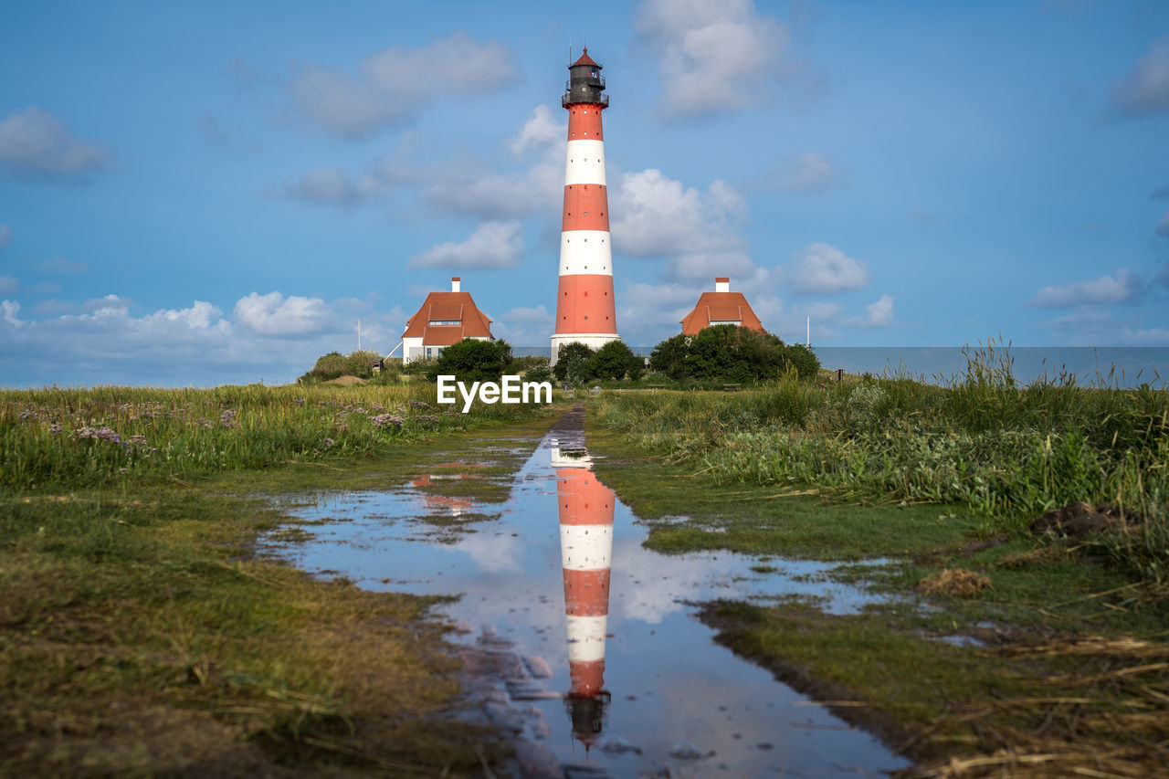 Lighthouse by building against sky