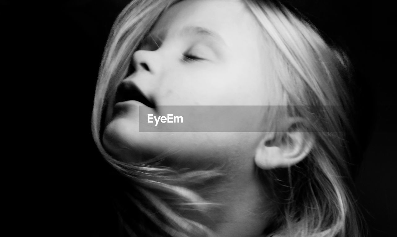 Close-up of girl with eyes closed against black background