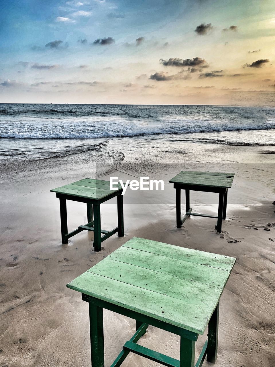EMPTY CHAIRS AND TABLES ON BEACH AGAINST SKY