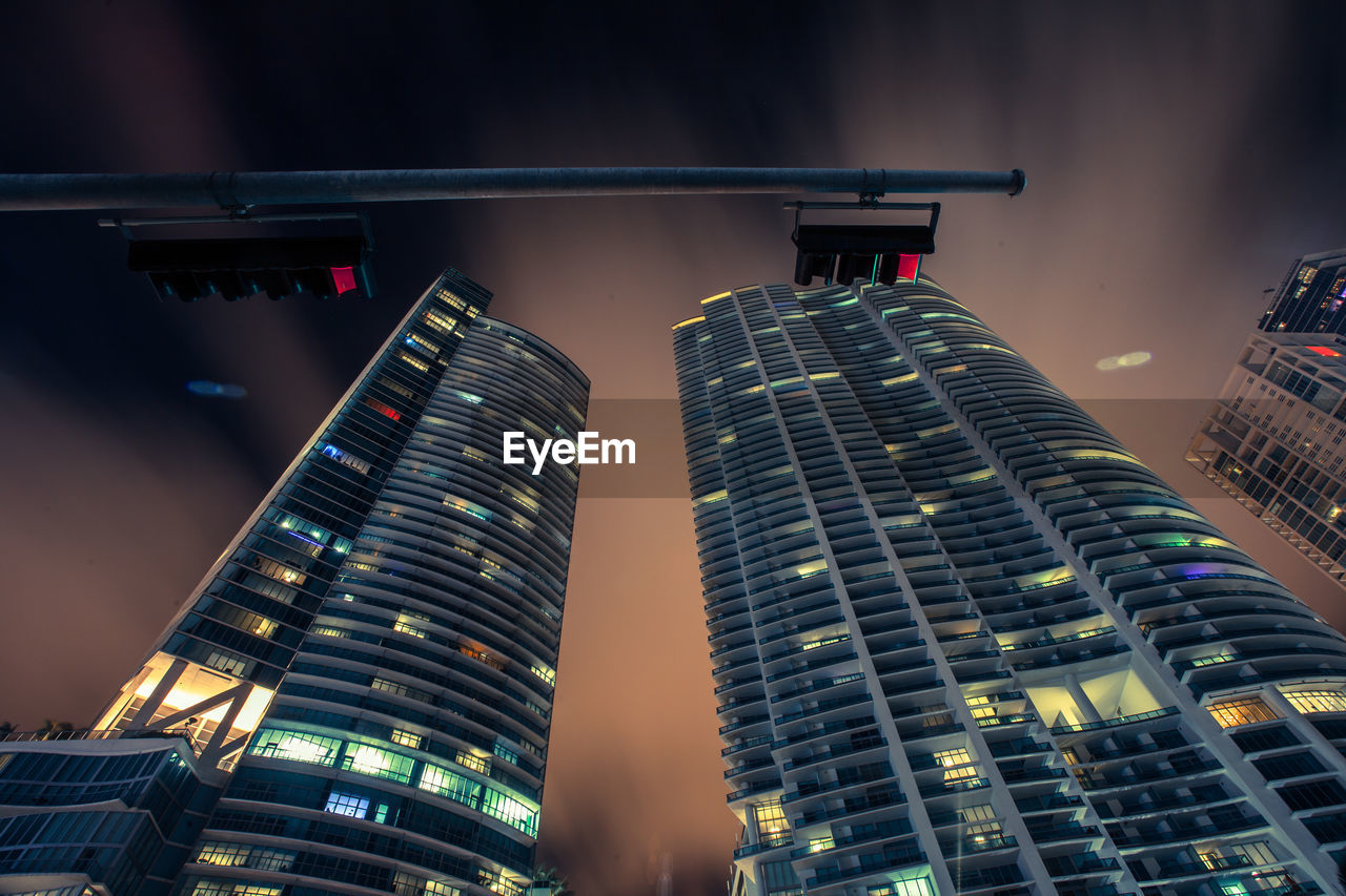 Low angle view of illuminated modern skyscrapers against cloudy sky