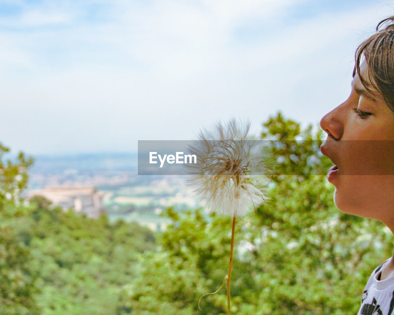 Close-up of boy blowing dandelion against sky