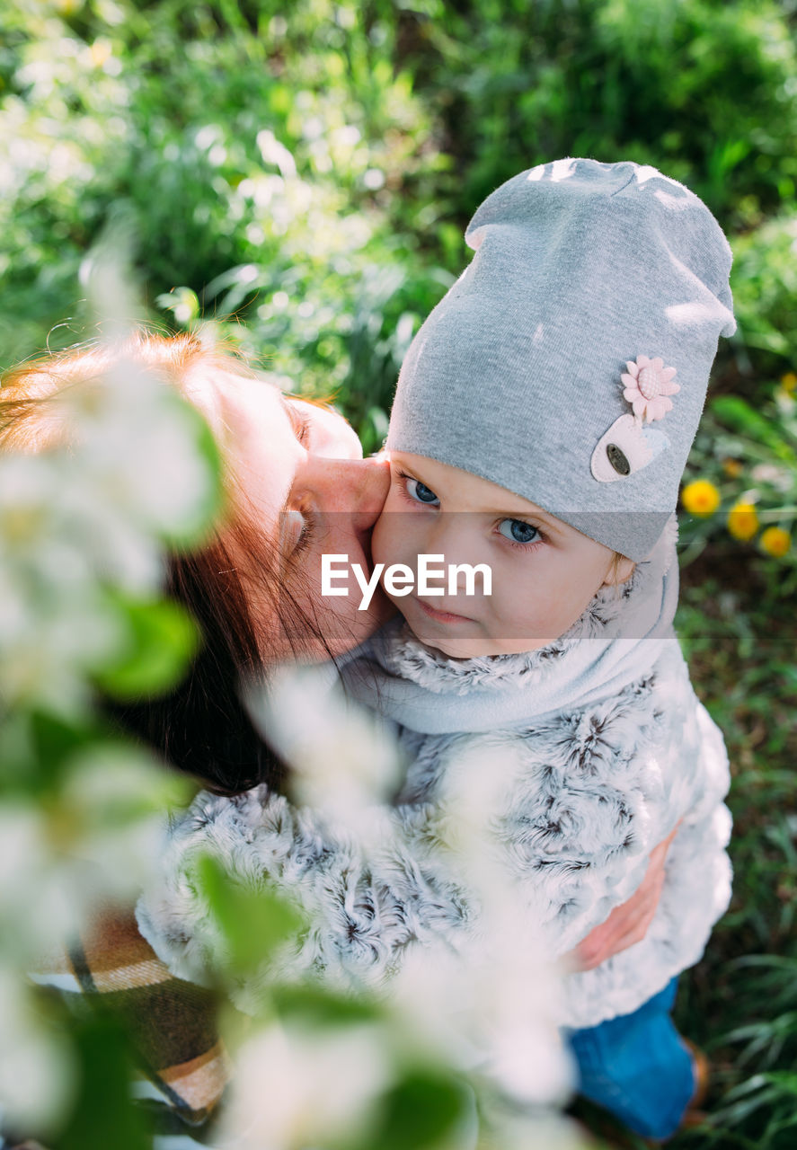 Young woman with her daughter in nature admires white flowering of spring trees