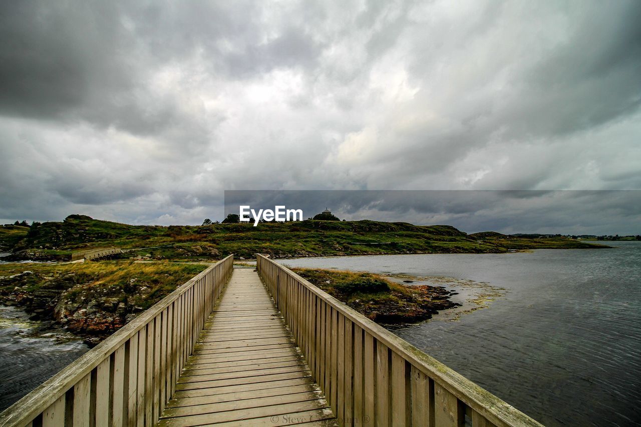 Footbridge over lake against sky