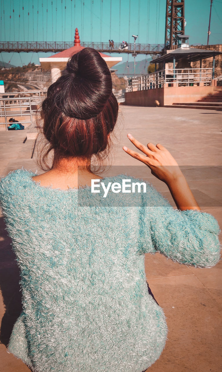 Rear view of woman gesturing peace sign while sitting in city