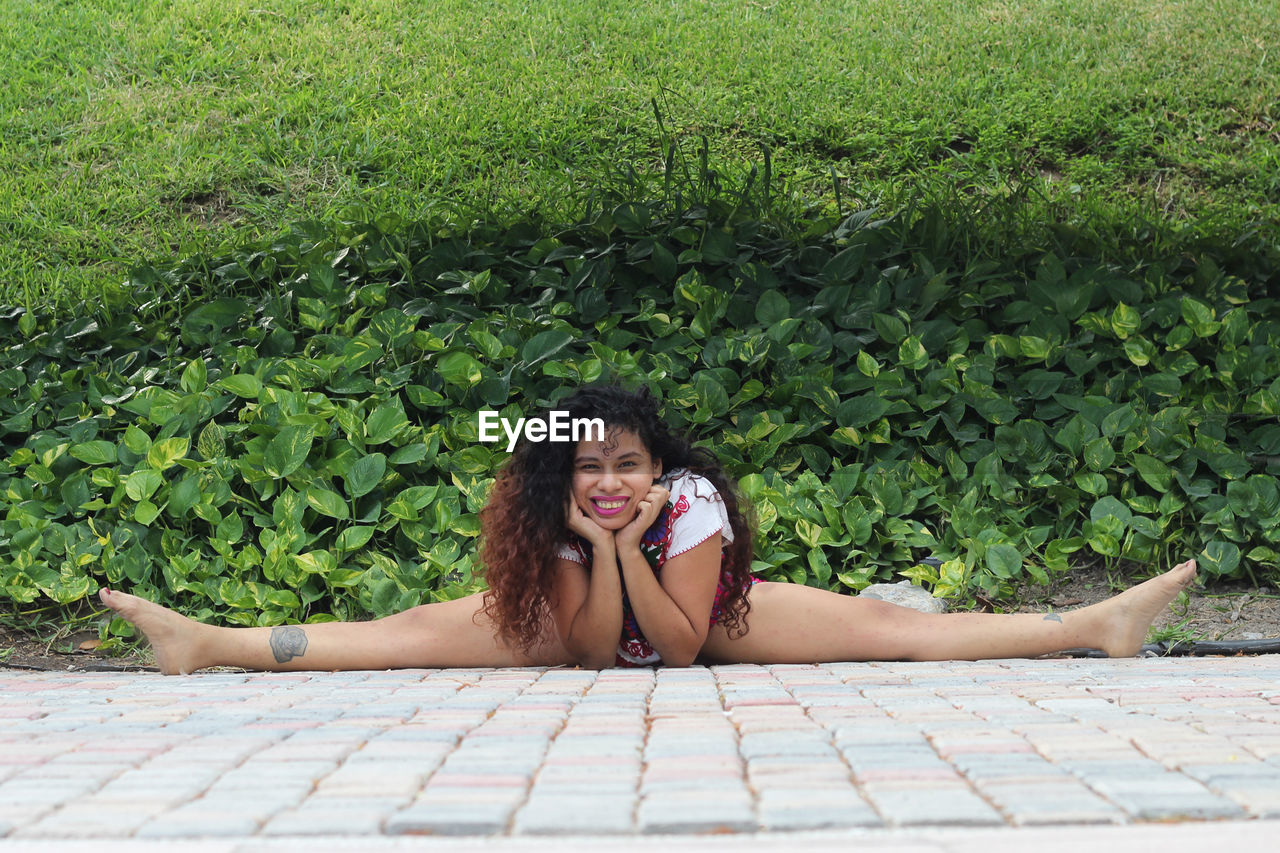 Portrait of woman doing splits on floor against plants