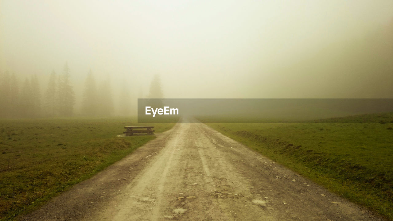 Country road amidst field against sky during foggy weather