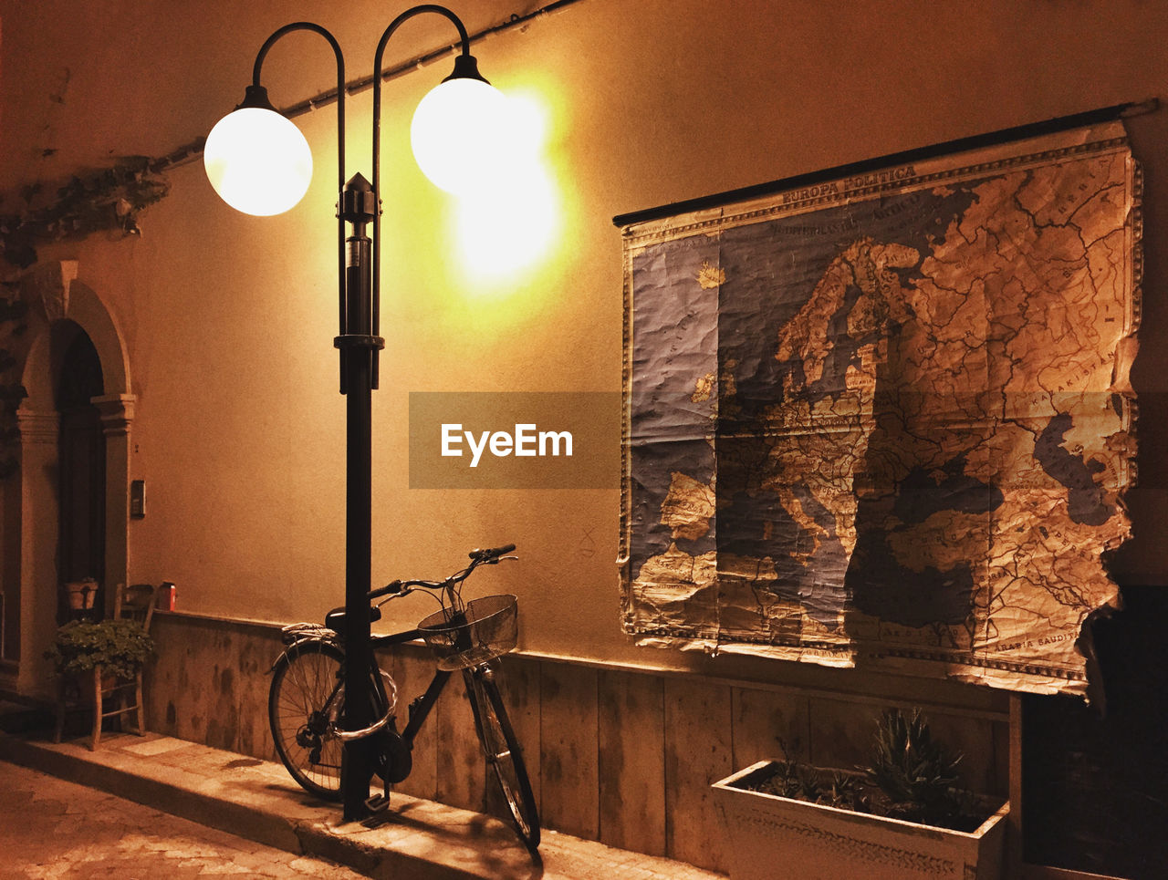 Bicycle parked by illuminated street light on sidewalk at night