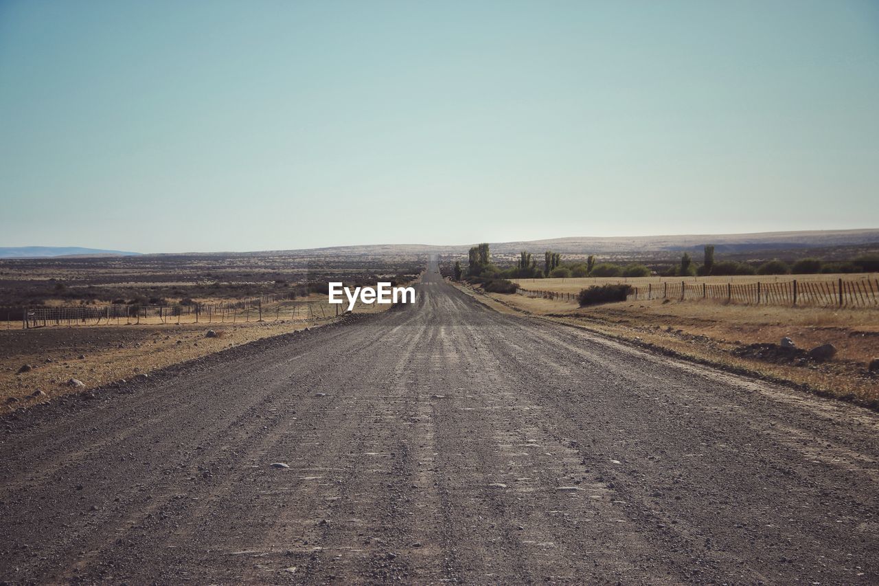 Road amidst field against clear sky