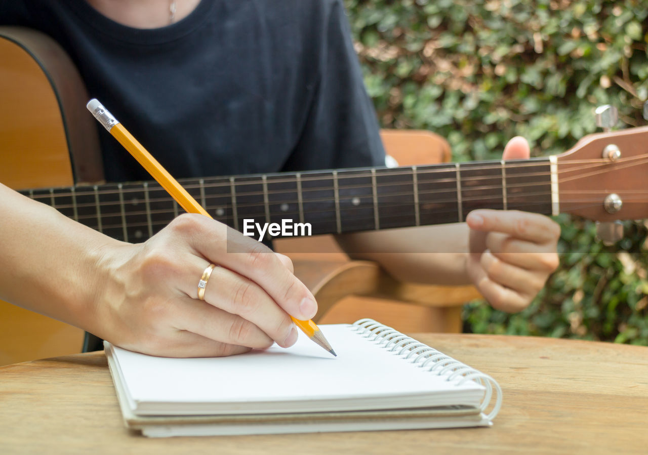 Midsection of men writing on diary while playing guitar