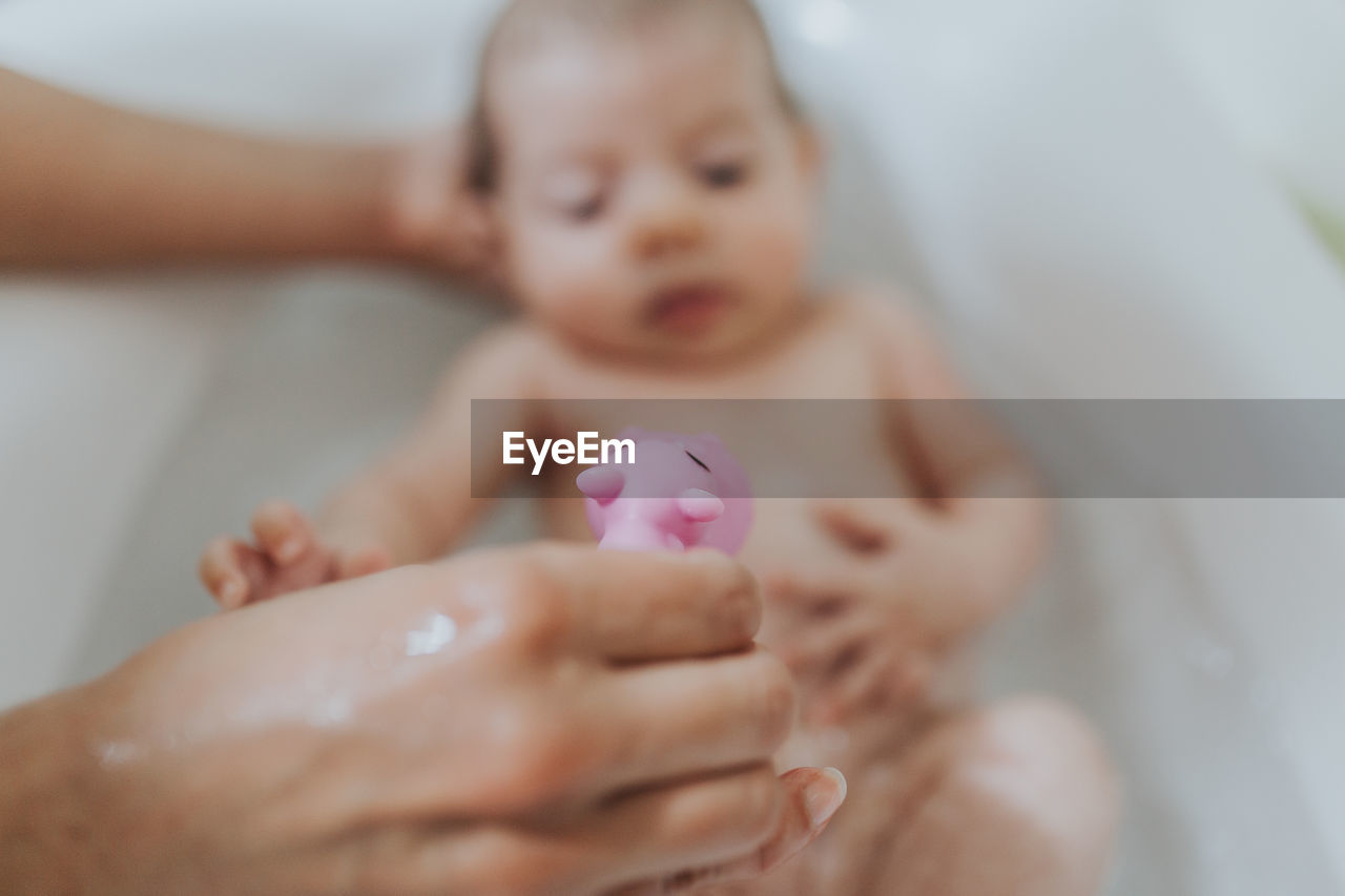 Cropped hands bathing baby girl in bathtub at home