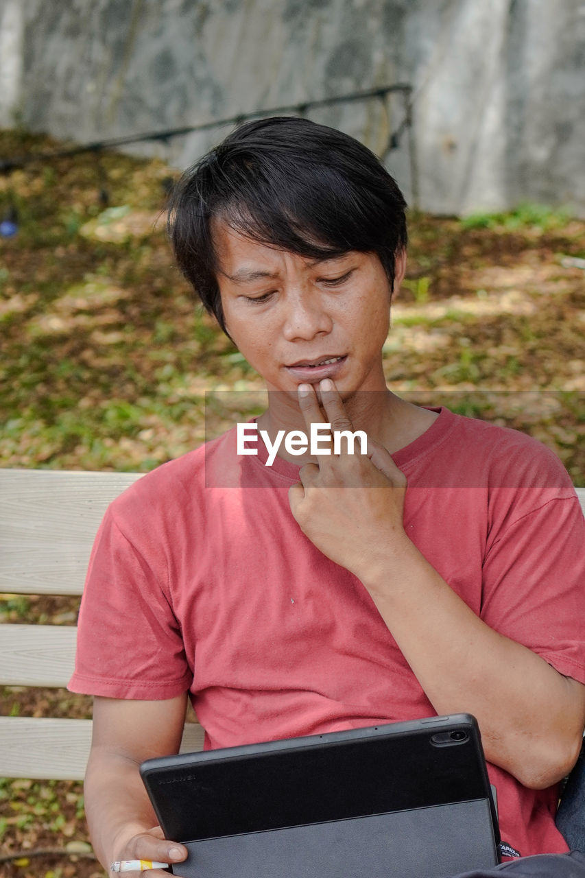 young woman using digital tablet while sitting outdoors