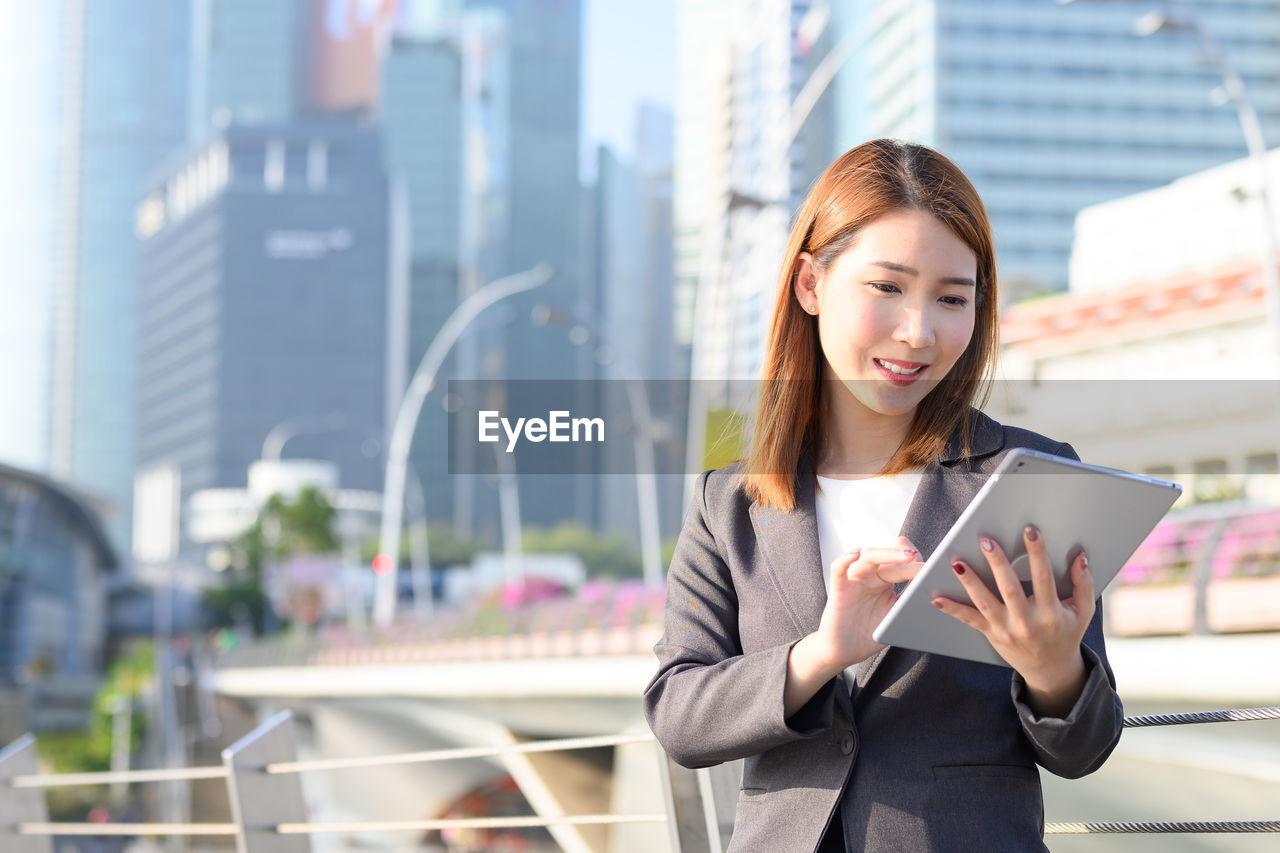 Businesswoman using digital tablet while standing in city