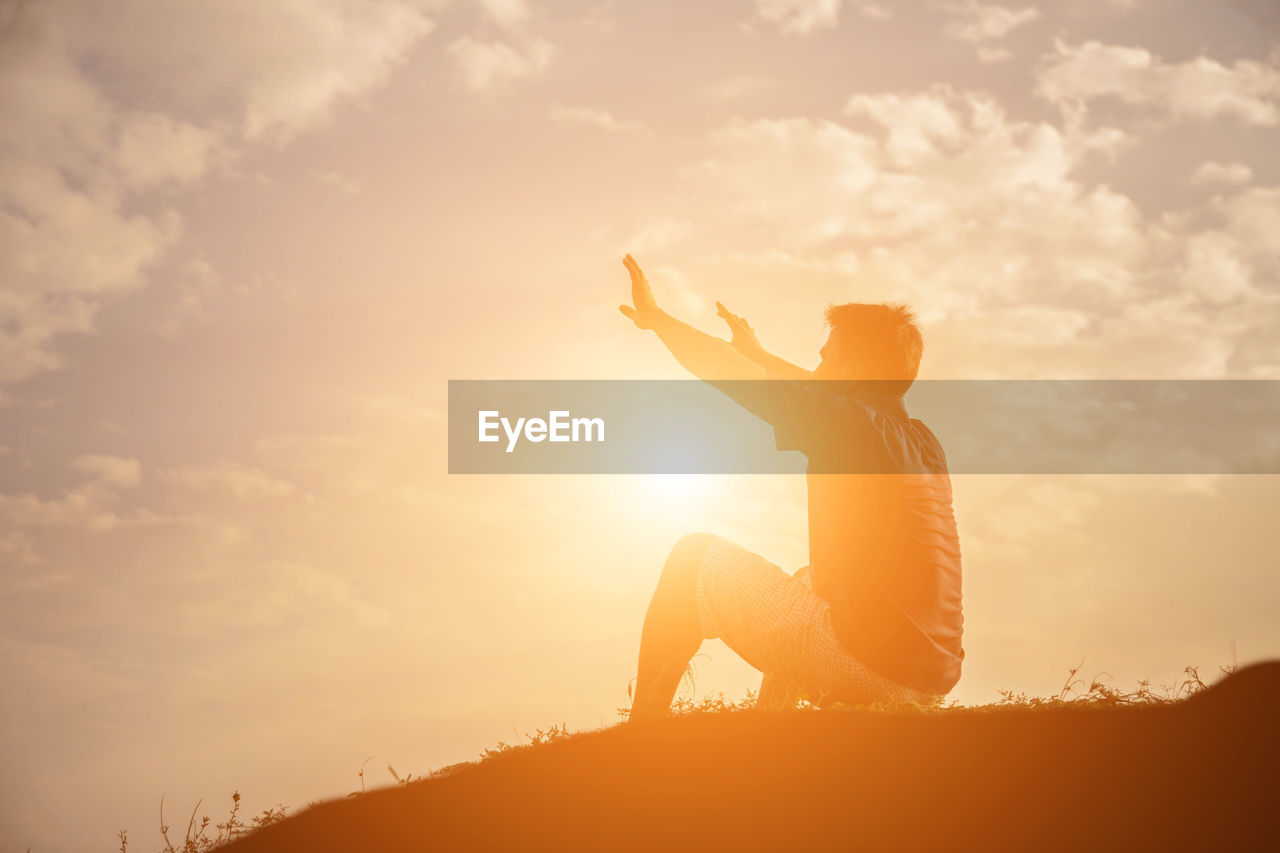 Side view of silhouette man sitting against sky during sunset