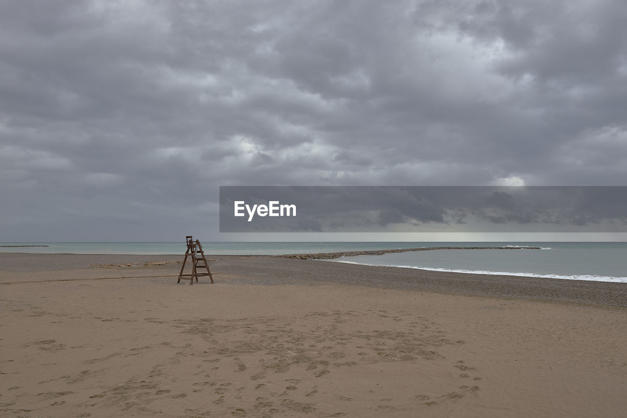 rear view of man walking at beach against cloudy sky