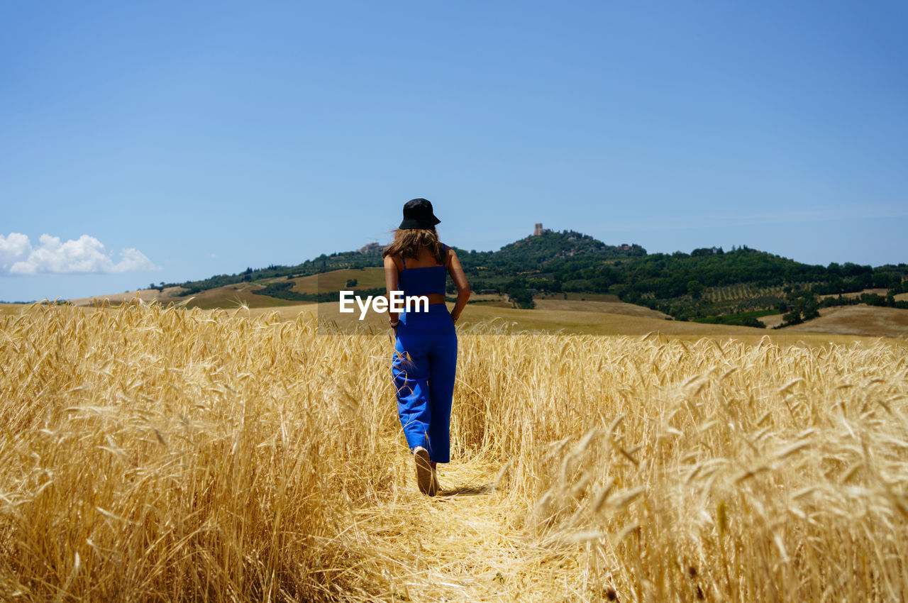 Girl walking through wheat fields in tuscany