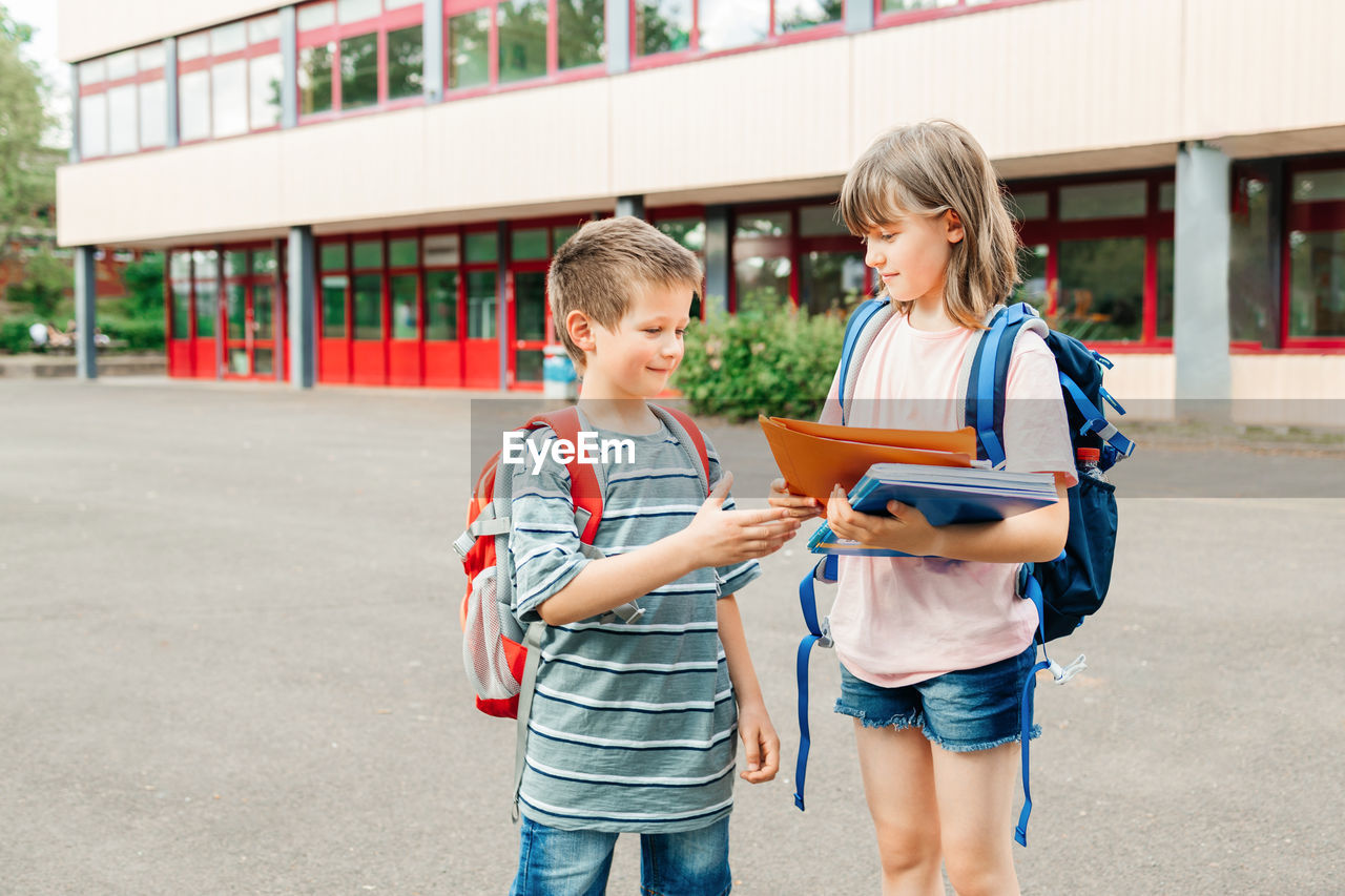 To school. brother and sister with school bags in the school yard. girl explaining homework 