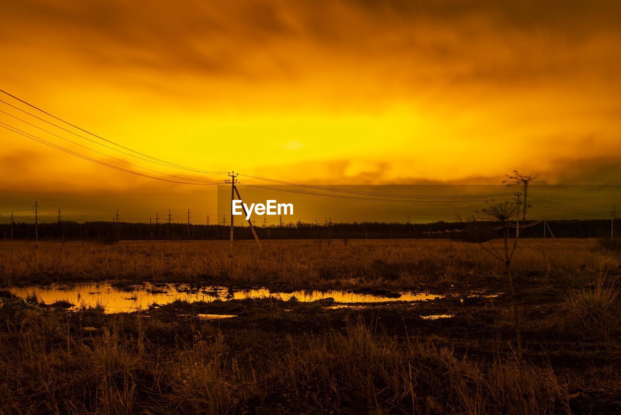 ELECTRICITY PYLON ON FIELD AGAINST SKY DURING SUNSET