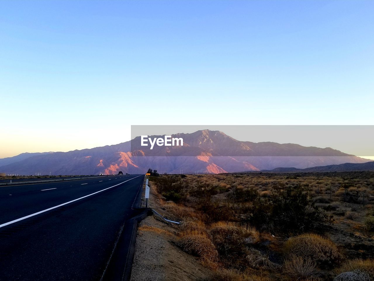 Road leading towards mountains against clear blue sky