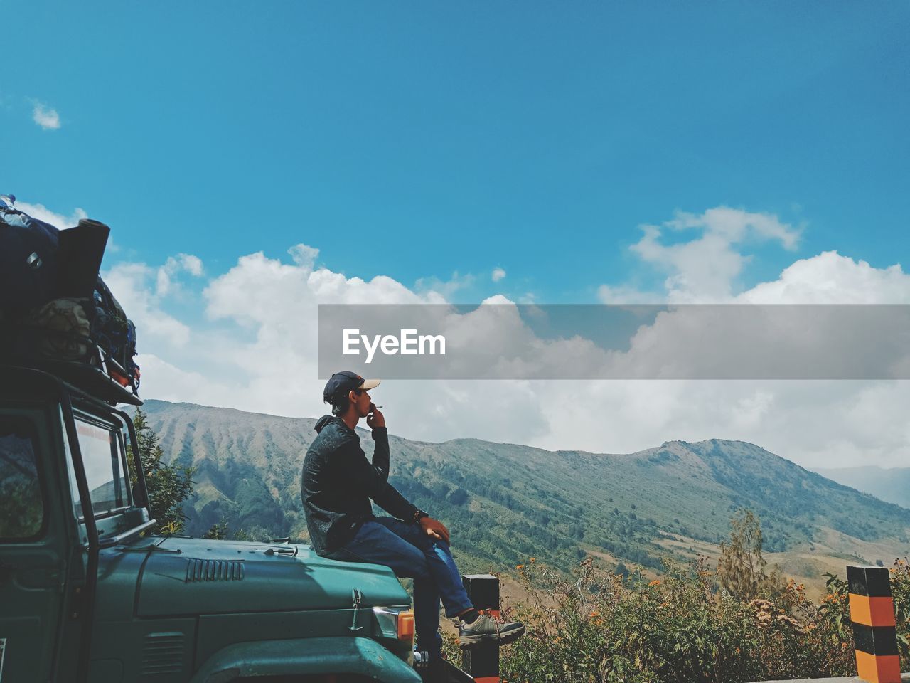 Man sitting on vehicle at mountain against sky