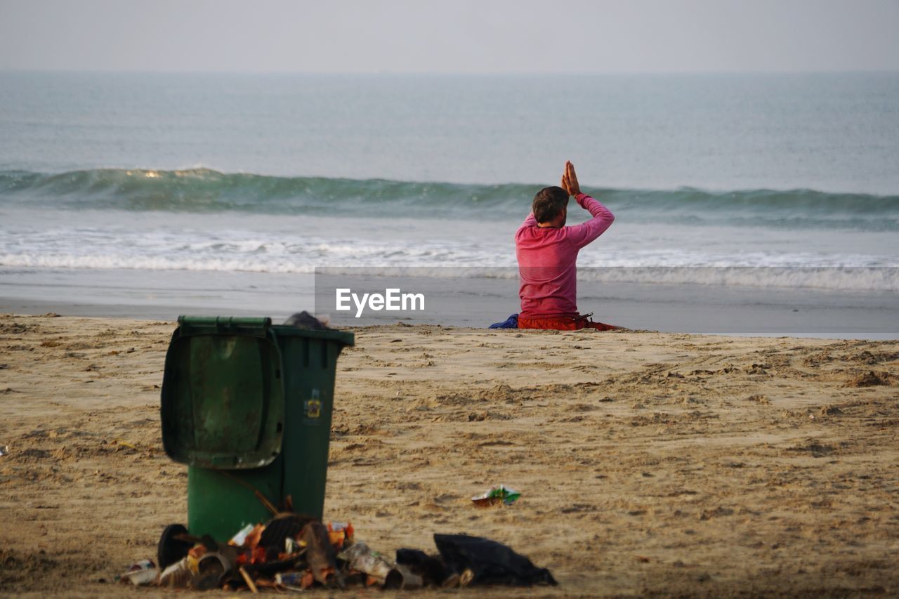 Rear view of man with hands clasped sitting at beach