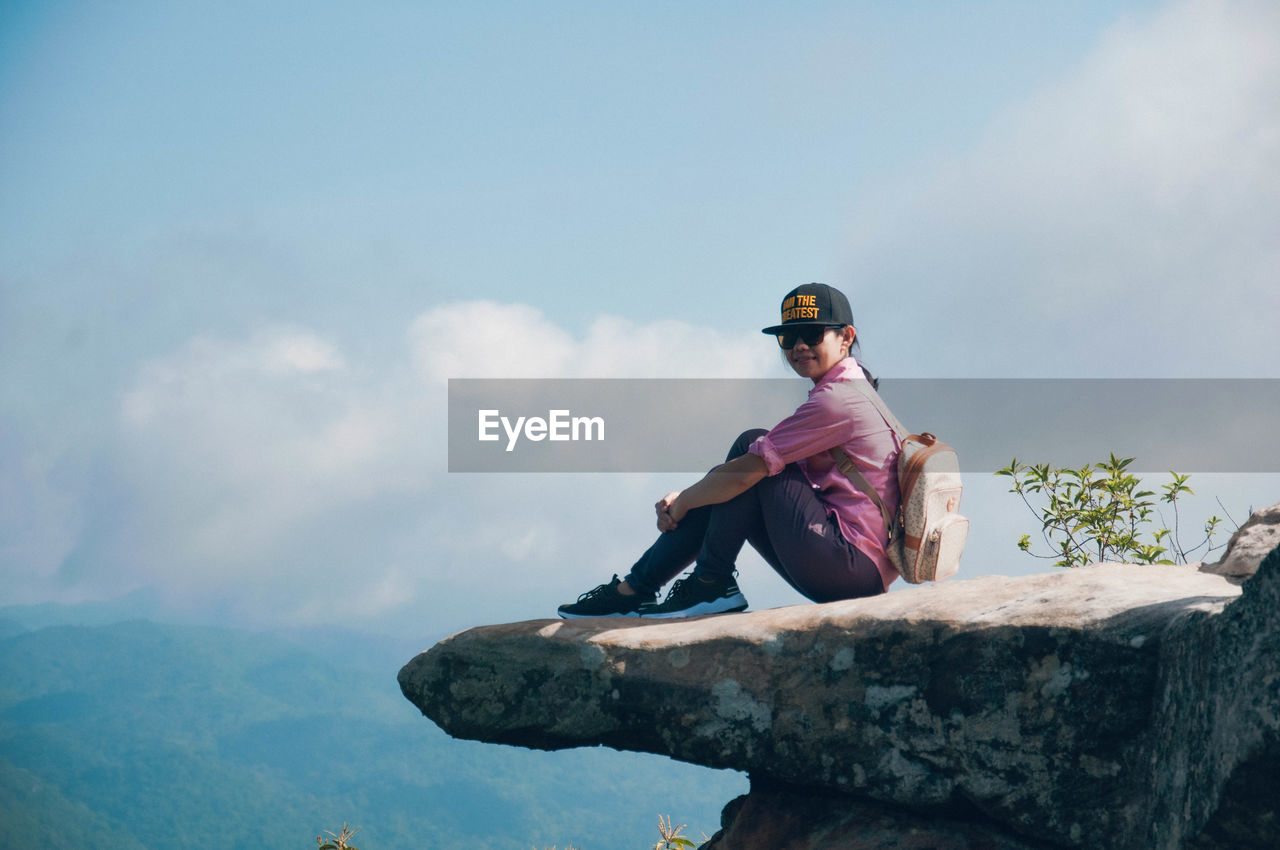 Portrait of woman sitting on rock against sky