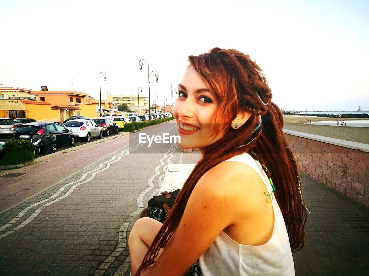 PORTRAIT OF SMILING YOUNG WOMAN STANDING ON ROAD IN CITY