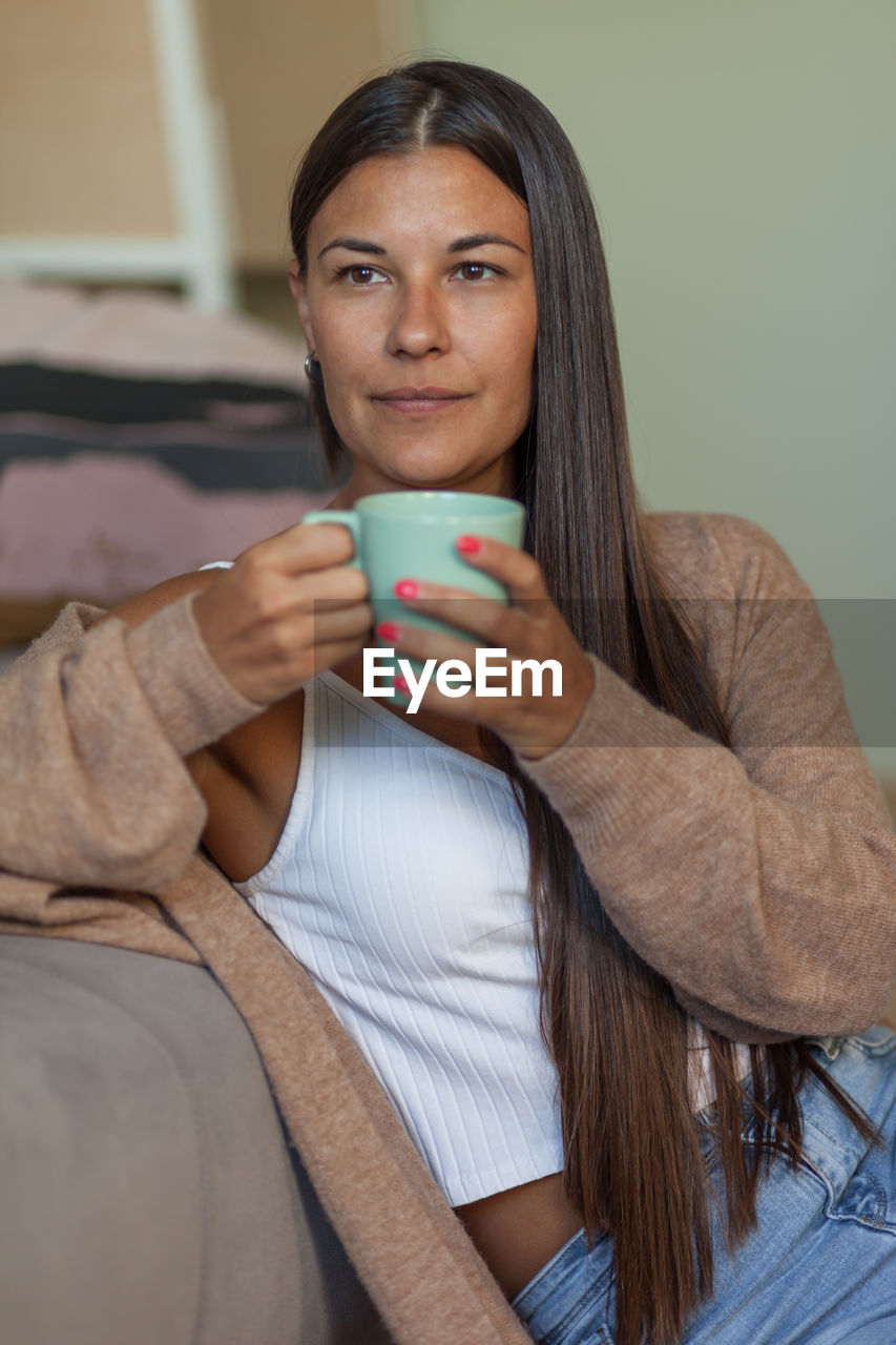 Smiling woman holding coffee cup while sitting on sofa at home