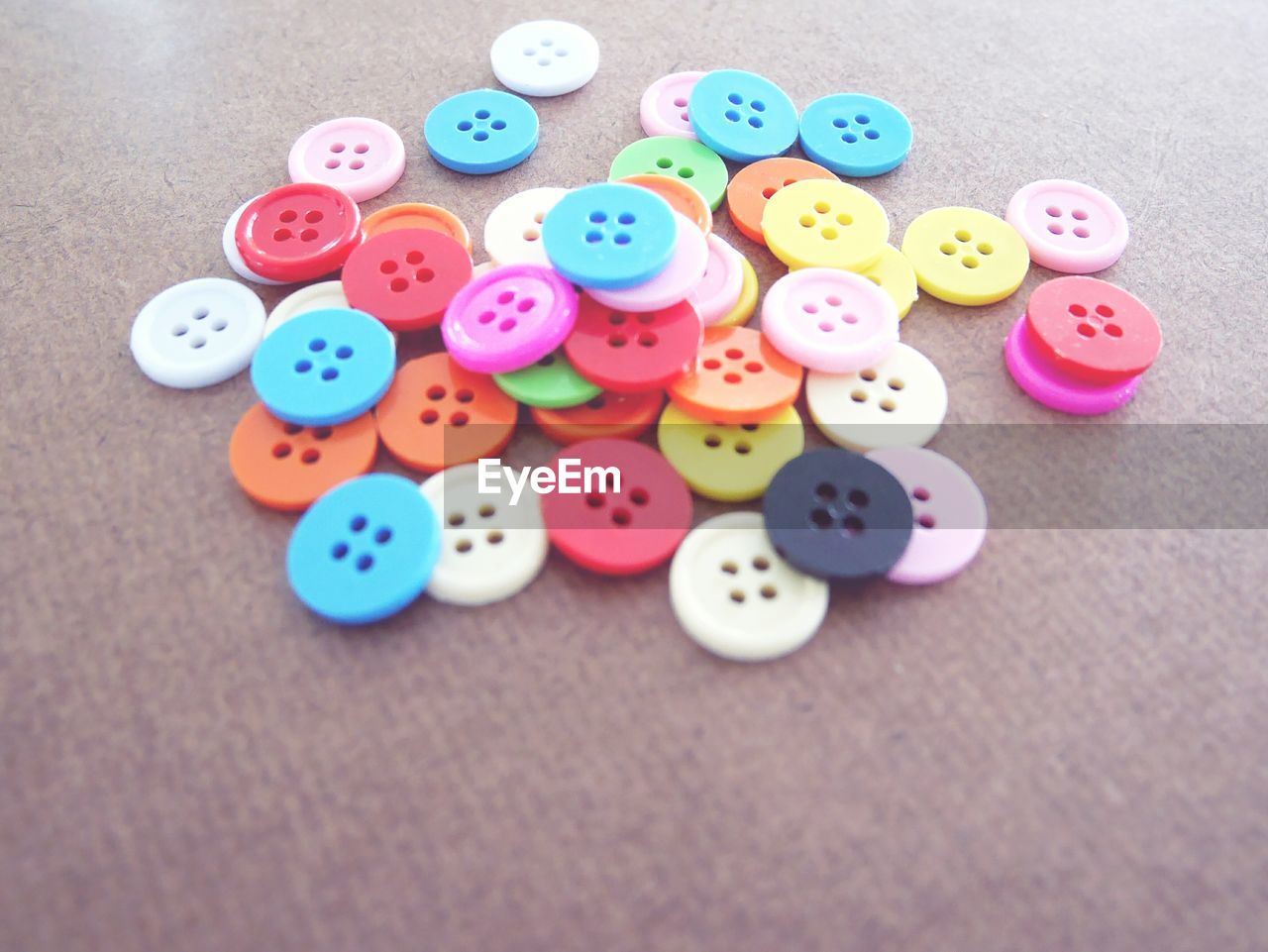 CLOSE-UP HIGH ANGLE VIEW OF MULTI COLORED BUTTONS ON PAPER