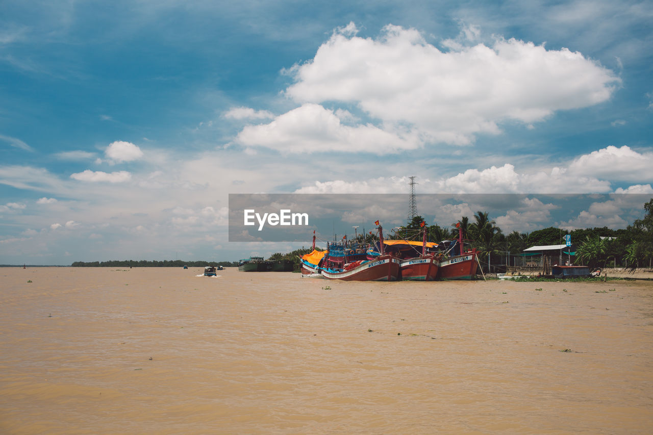 Fishing boats moored in river against sky