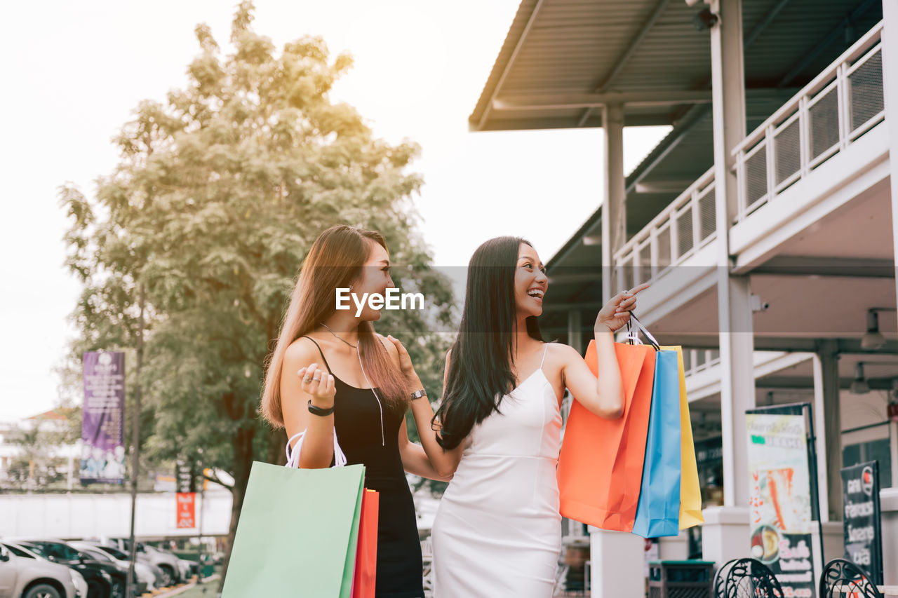 Happy friends with colorful shopping bags while standing on street in city