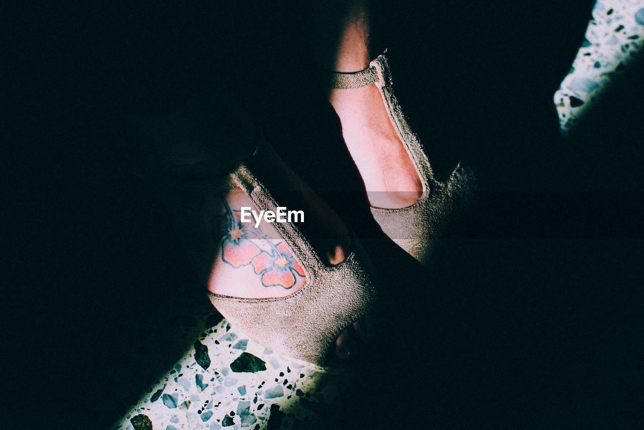 Low section of woman wearing shoes with flower tattoo