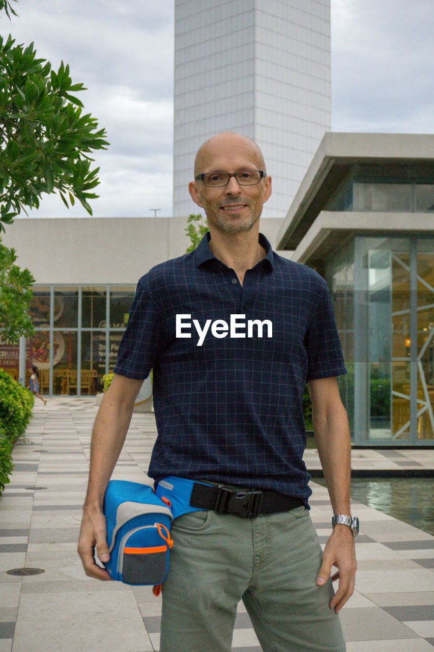 PORTRAIT OF MAN STANDING AGAINST MODERN BUILDING