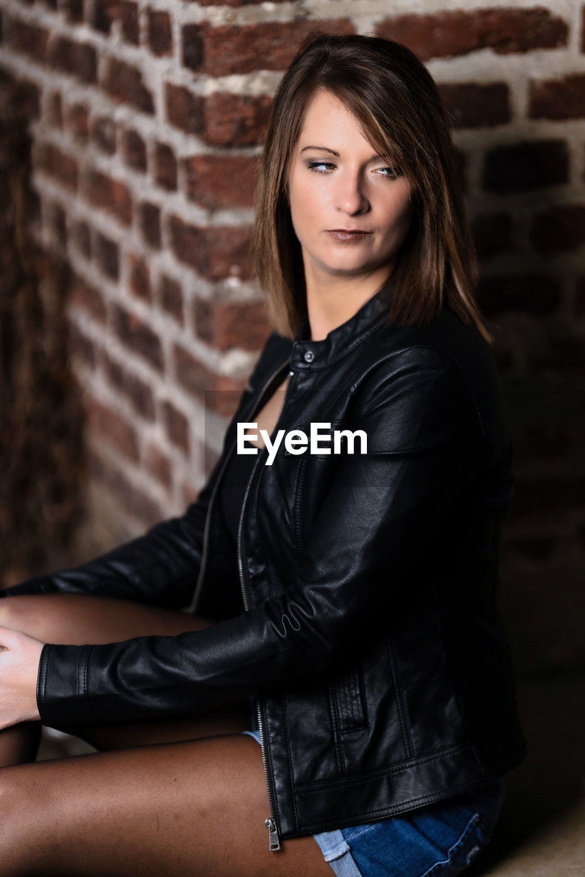 brick, brick wall, adult, women, young adult, one person, portrait, leather, wall, hairstyle, looking at camera, leather jacket, long hair, clothing, fashion, black, brown hair, sitting, photo shoot, female, lifestyles, jacket, wall - building feature, relaxation, casual clothing, three quarter length, architecture, indoors, emotion, human leg, portrait photography, person