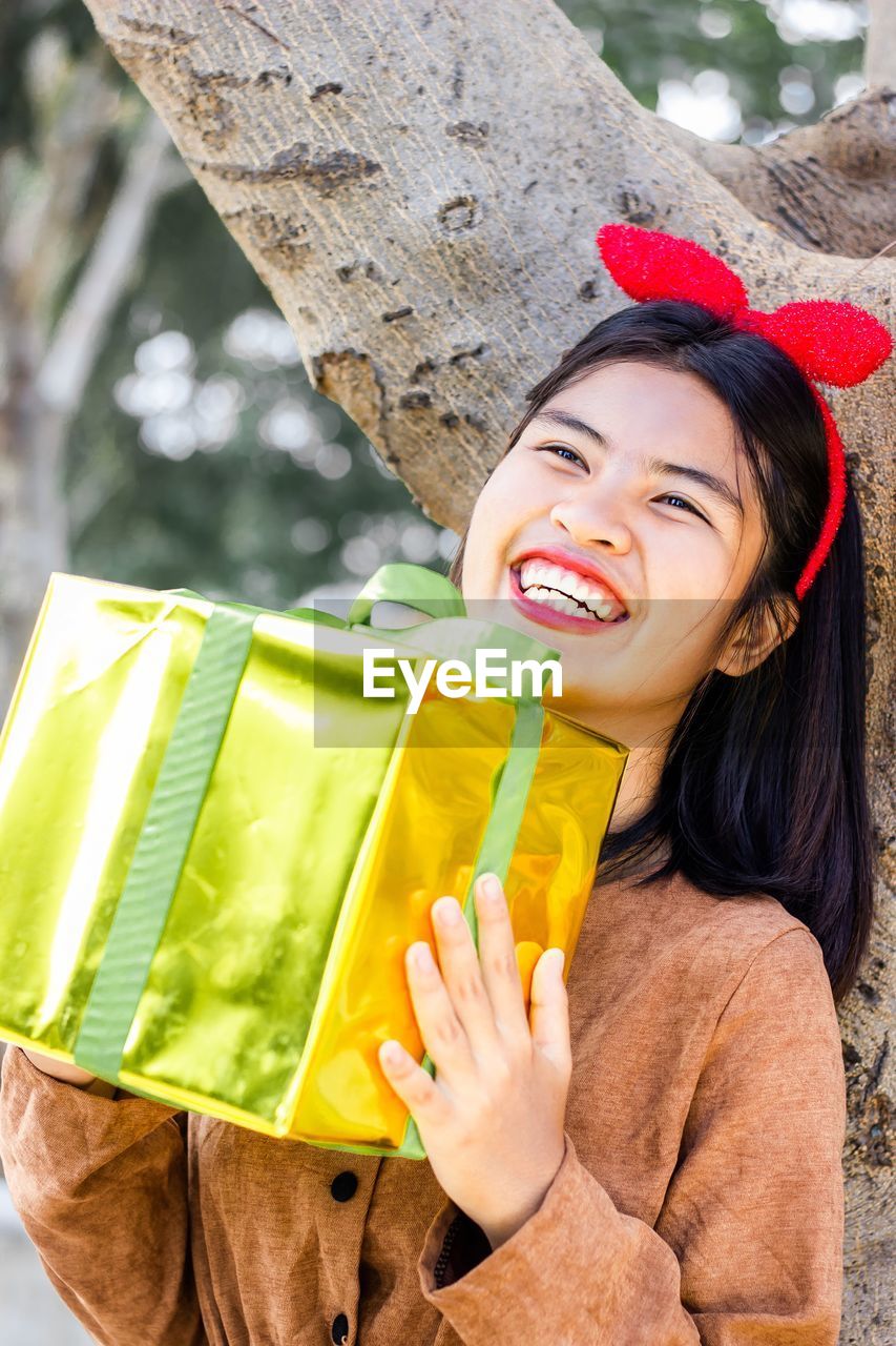 Cheerful attractive young woman holding christmas or new year decorated gold gift box.