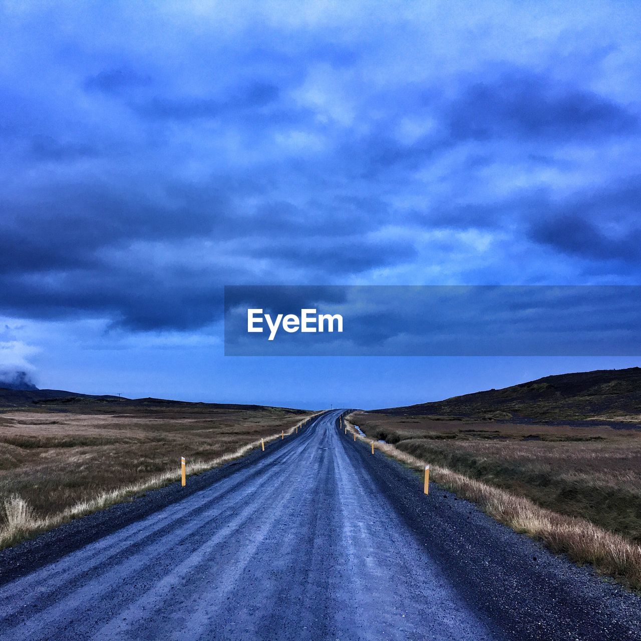 Road passing through field against cloudy sky