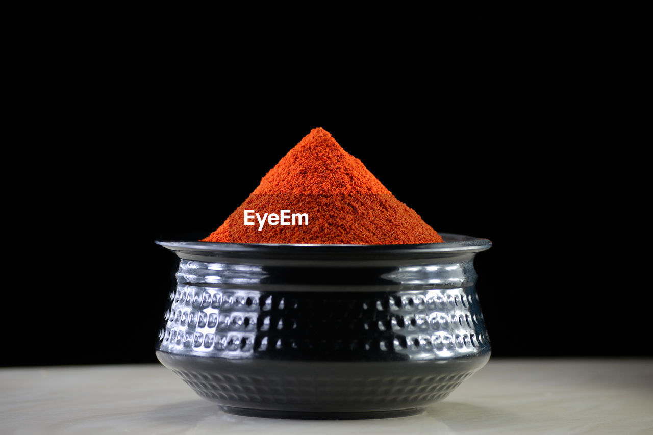 Red chili powder in black bowl on dark background