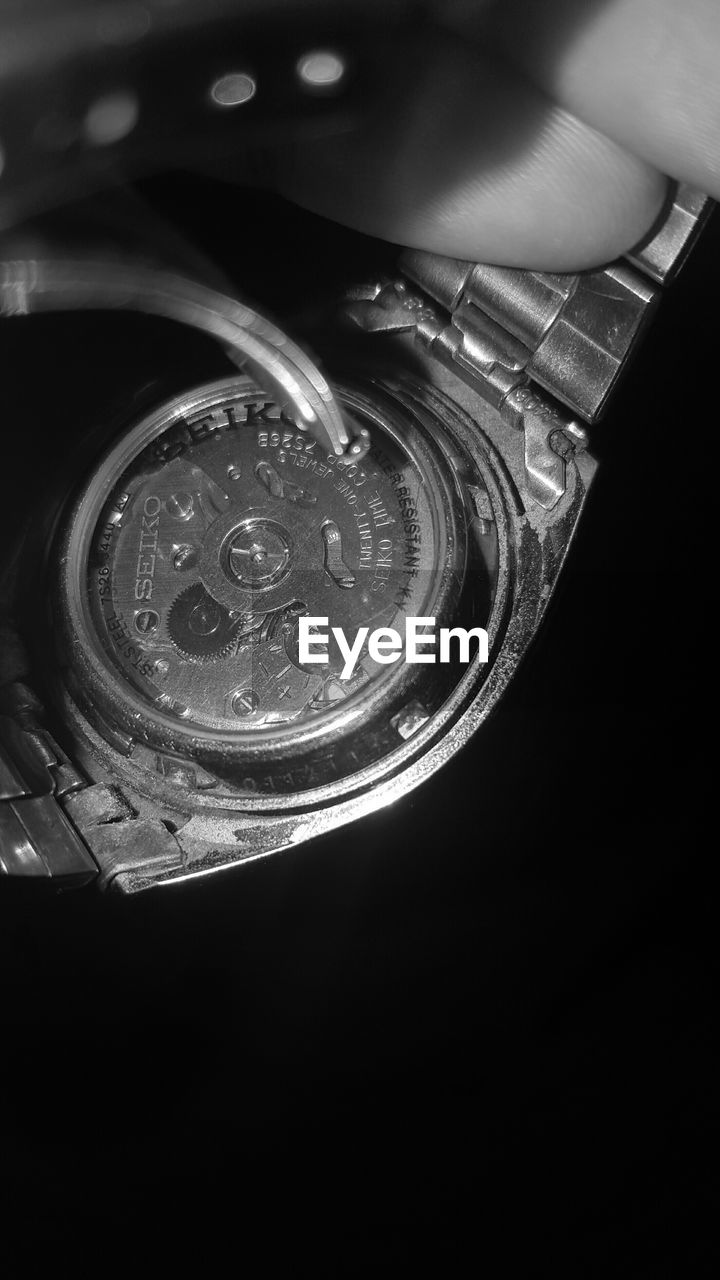 Cropped image of hand holding wristwatch against black background