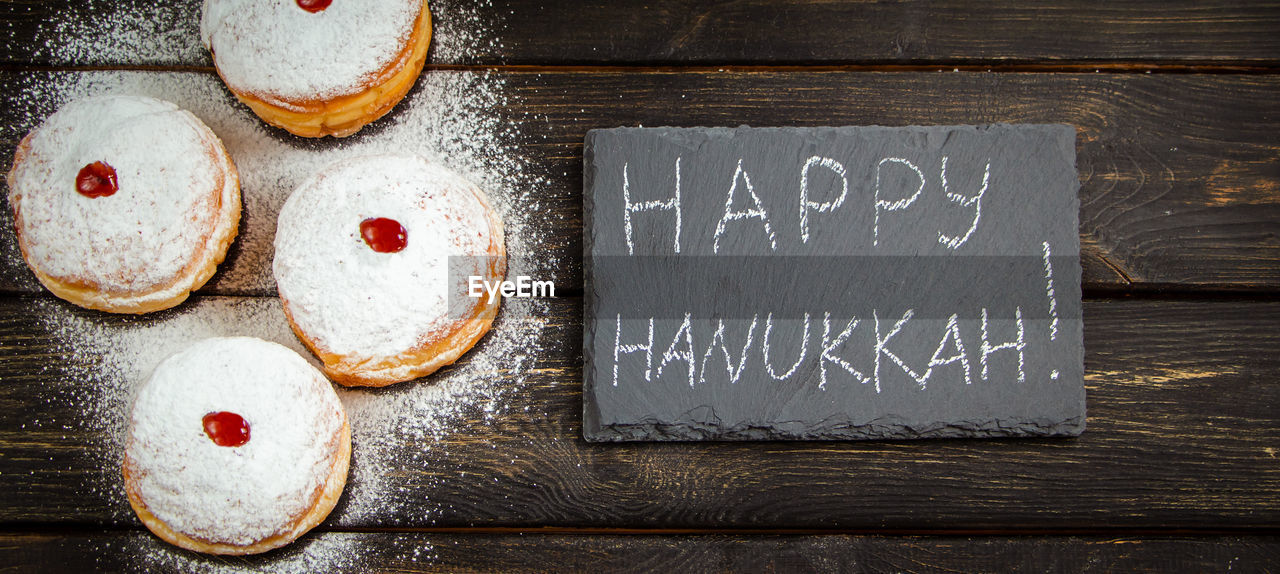 Happy hanukkah. traditional dessert sufganiyot on dark wooden background. donuts, candles and gifts