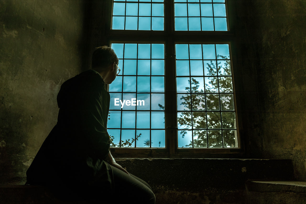 Side view of young man looking through window