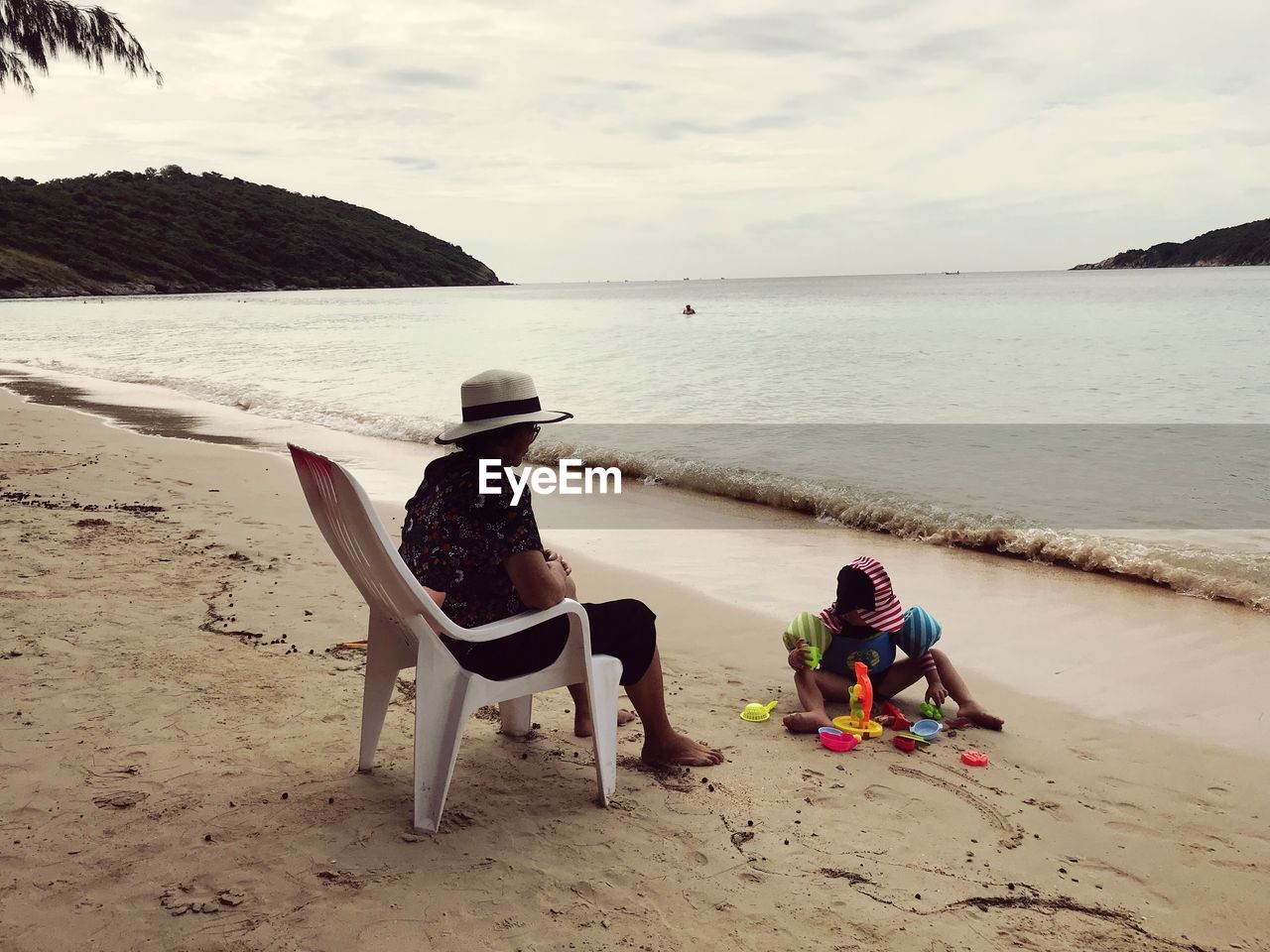 REAR VIEW OF MEN SITTING ON BEACH