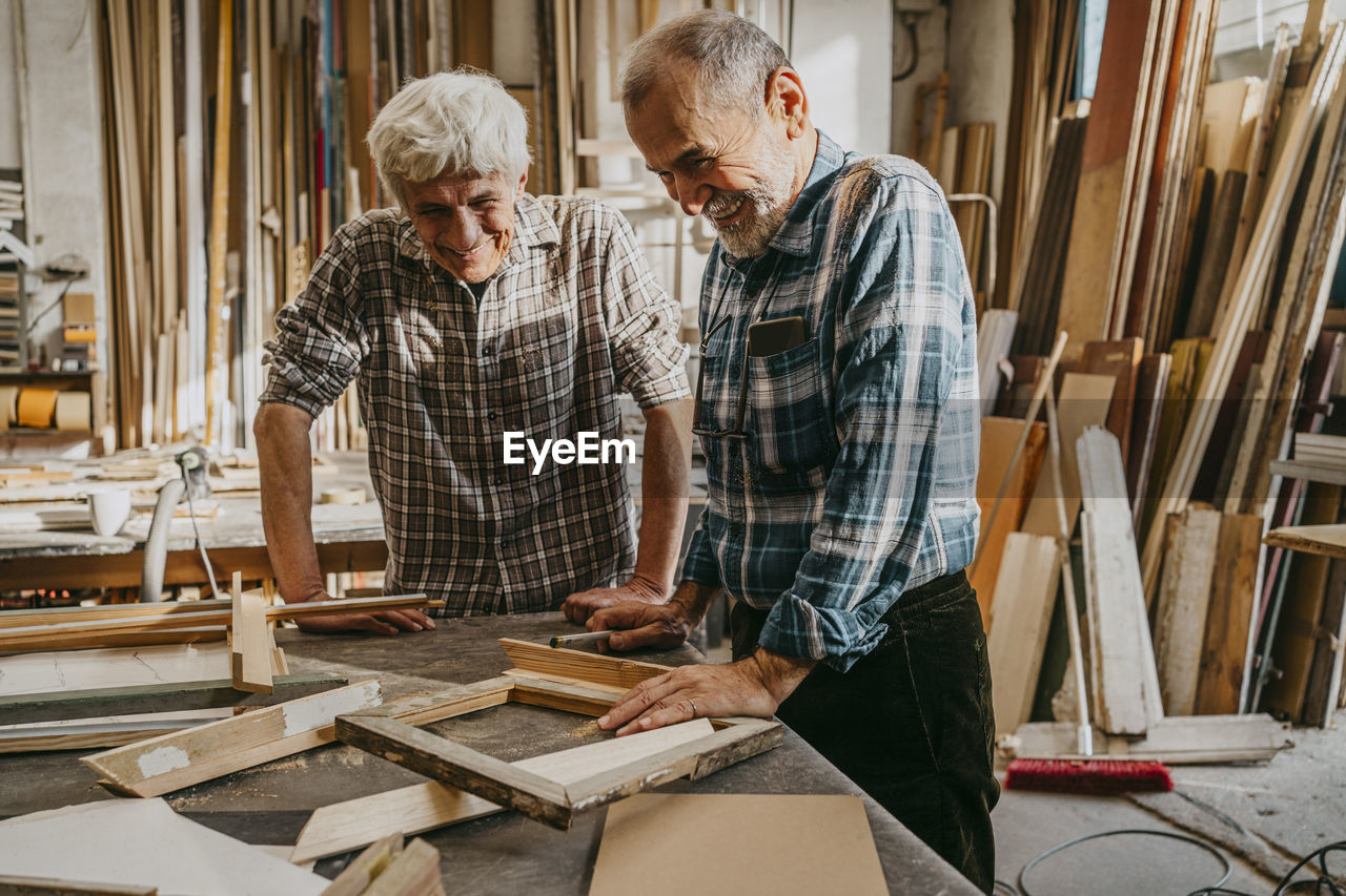Happy senior craftsmen looking at wooden frames at repair shop