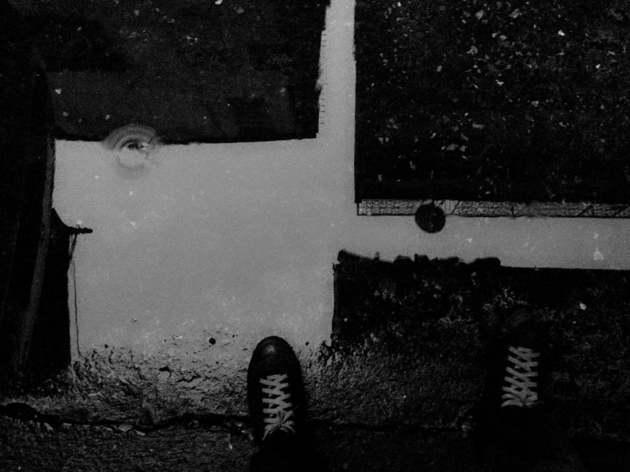 Low section of person standing by puddle with building reflection