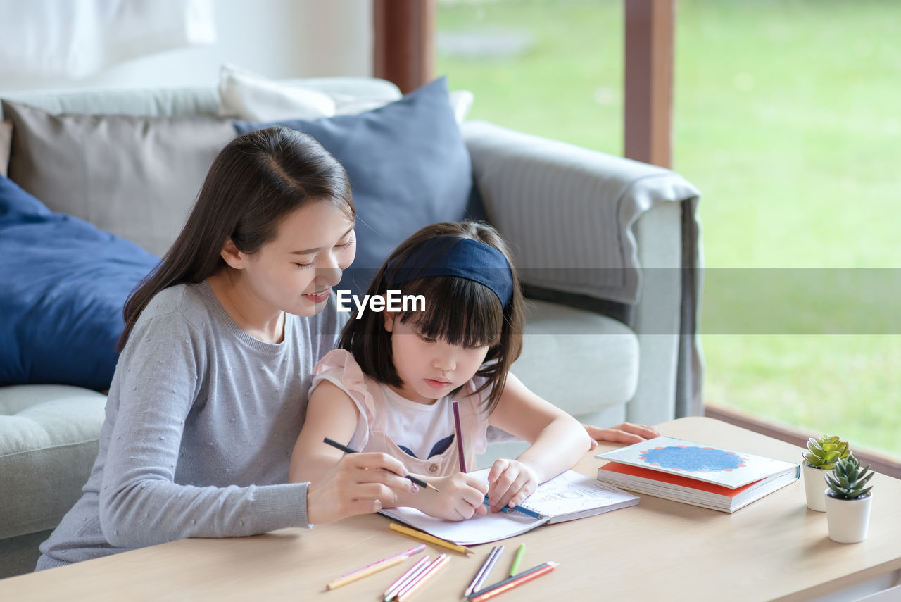 Asian mother teaching her cute kid daughter to studying in living room at home