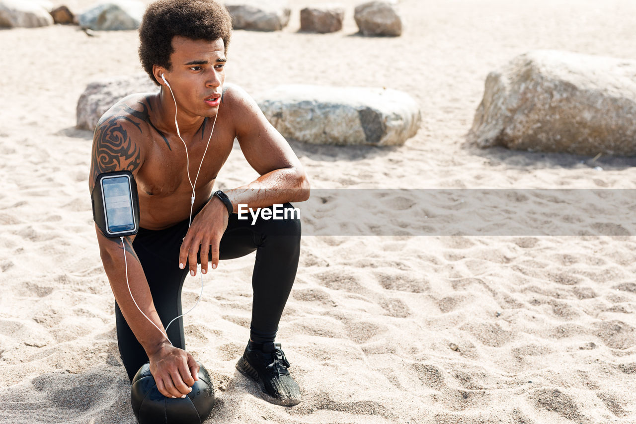 Shirtless young man looking away while relaxing on beach