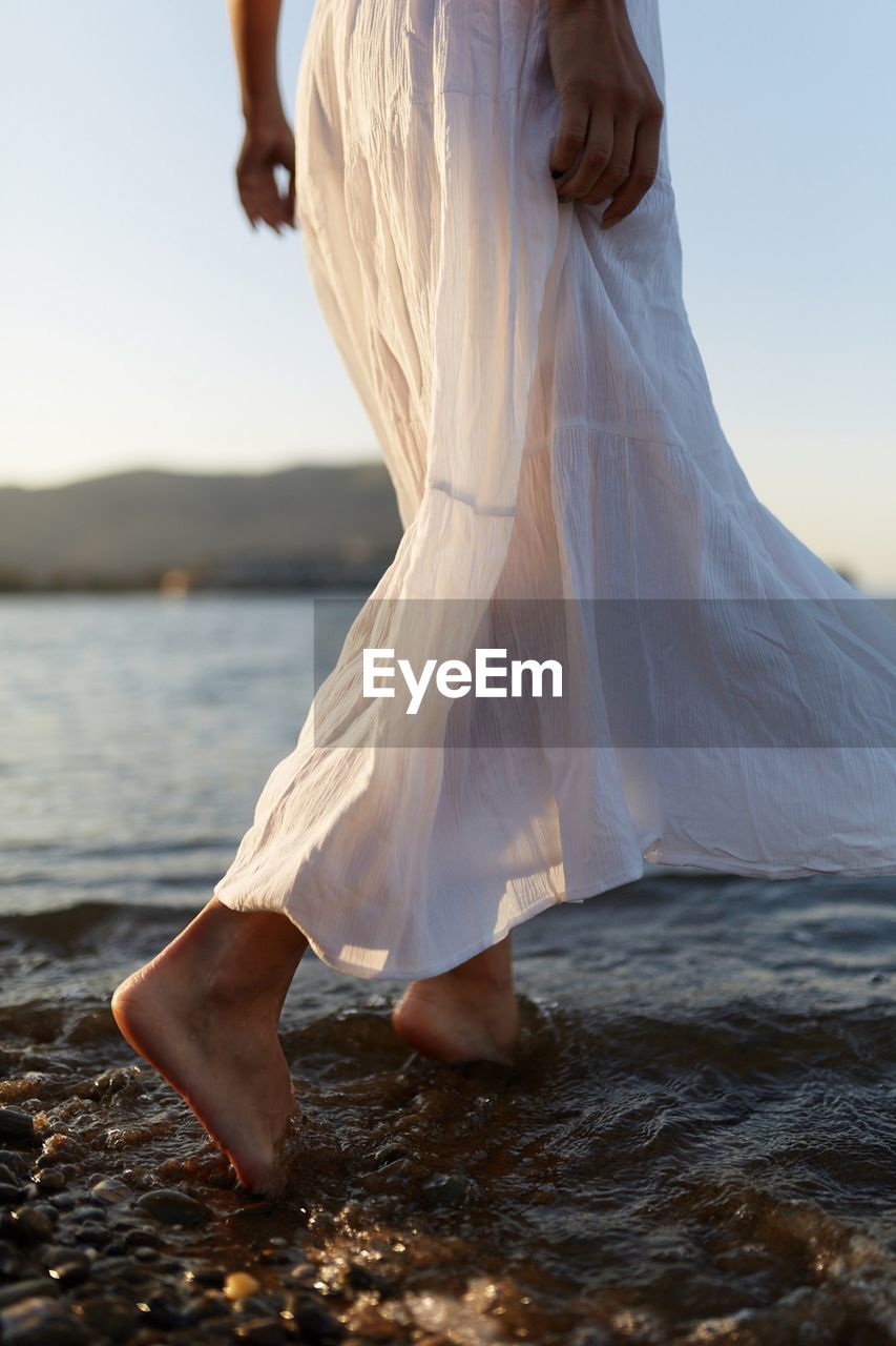 LOW SECTION OF WOMAN STANDING AT BEACH