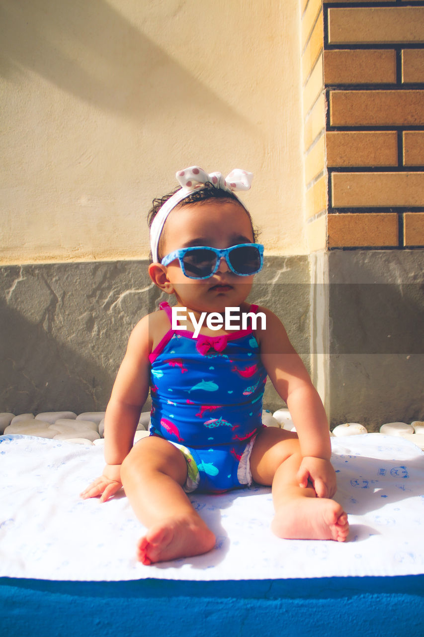 child, childhood, one person, sunglasses, full length, blue, sunlight, glasses, fashion, sitting, front view, toddler, day, innocence, leisure activity, portrait, men, fun, lifestyles, cute, happiness, summer, nature, smiling, female, architecture, outdoors, enjoyment, swimwear, emotion, clothing, baby, casual clothing, looking at camera, women, person, carefree, swimming